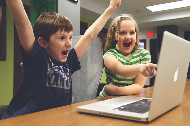 a young girl and boy cheer in front of a Mac as they play a video game